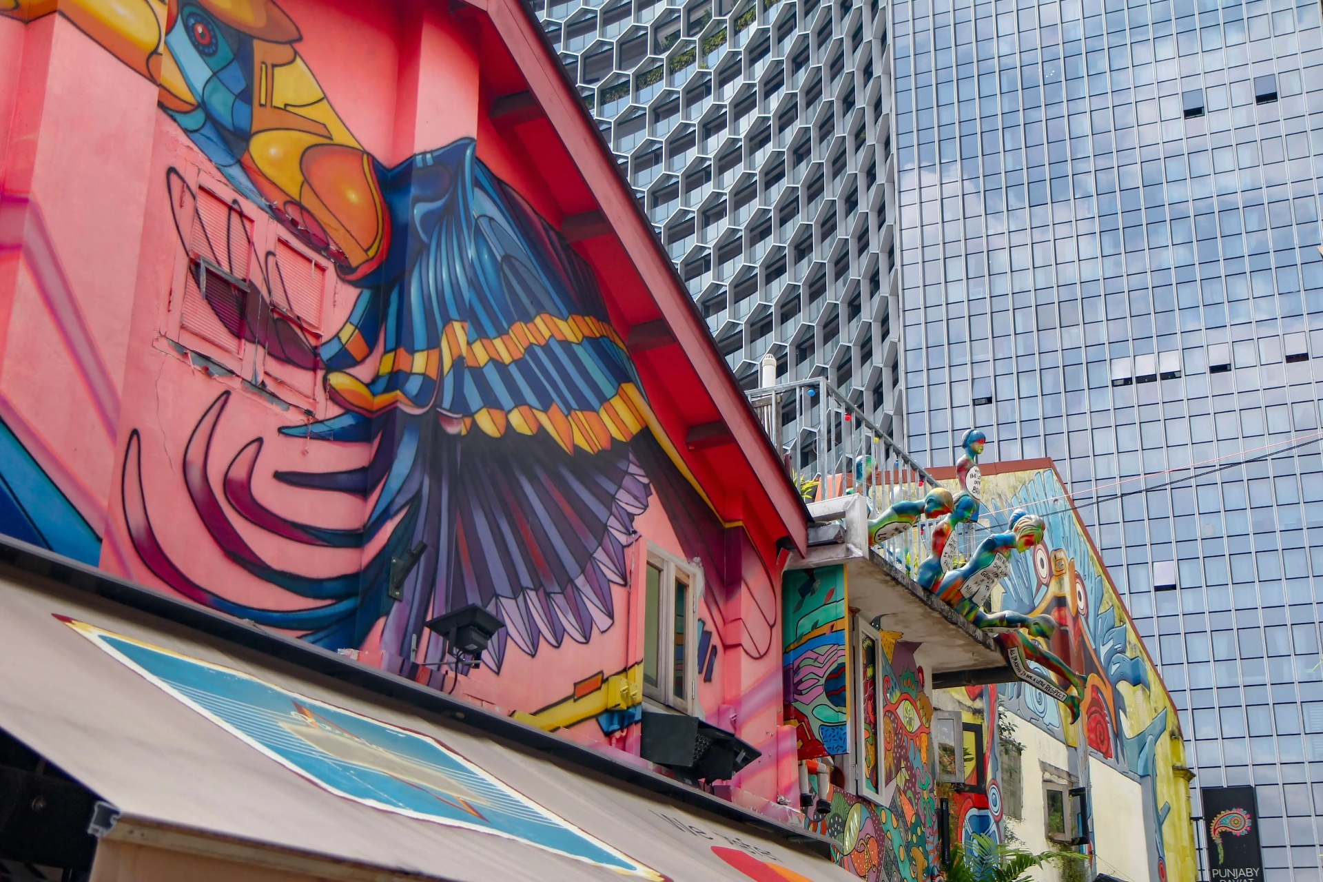 A brightly painted shophouse street of murals set against glass towers in Singapore